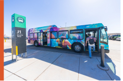 A photo of a DEN bus shuttle picking up a passenger at the airport parking lot area.