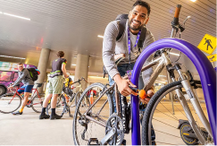 A photo of a person locking a bicycle up at the airport with two other cyclists in the background.