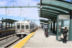 A photo of an A Line commuter rail train parked at a station near DEN with passengers on the platform under a cover. 