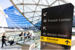 A photo of a wayfinding sign at the airport pointing to where the Transit Center is with the Westin Hotel in the background.